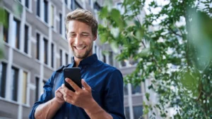 Ein Mann hantiert lächelnd an seinem Smartphone.