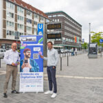 Zwei Personen stehen neben einem Werbeaufsteller für die Digitallinie 302.