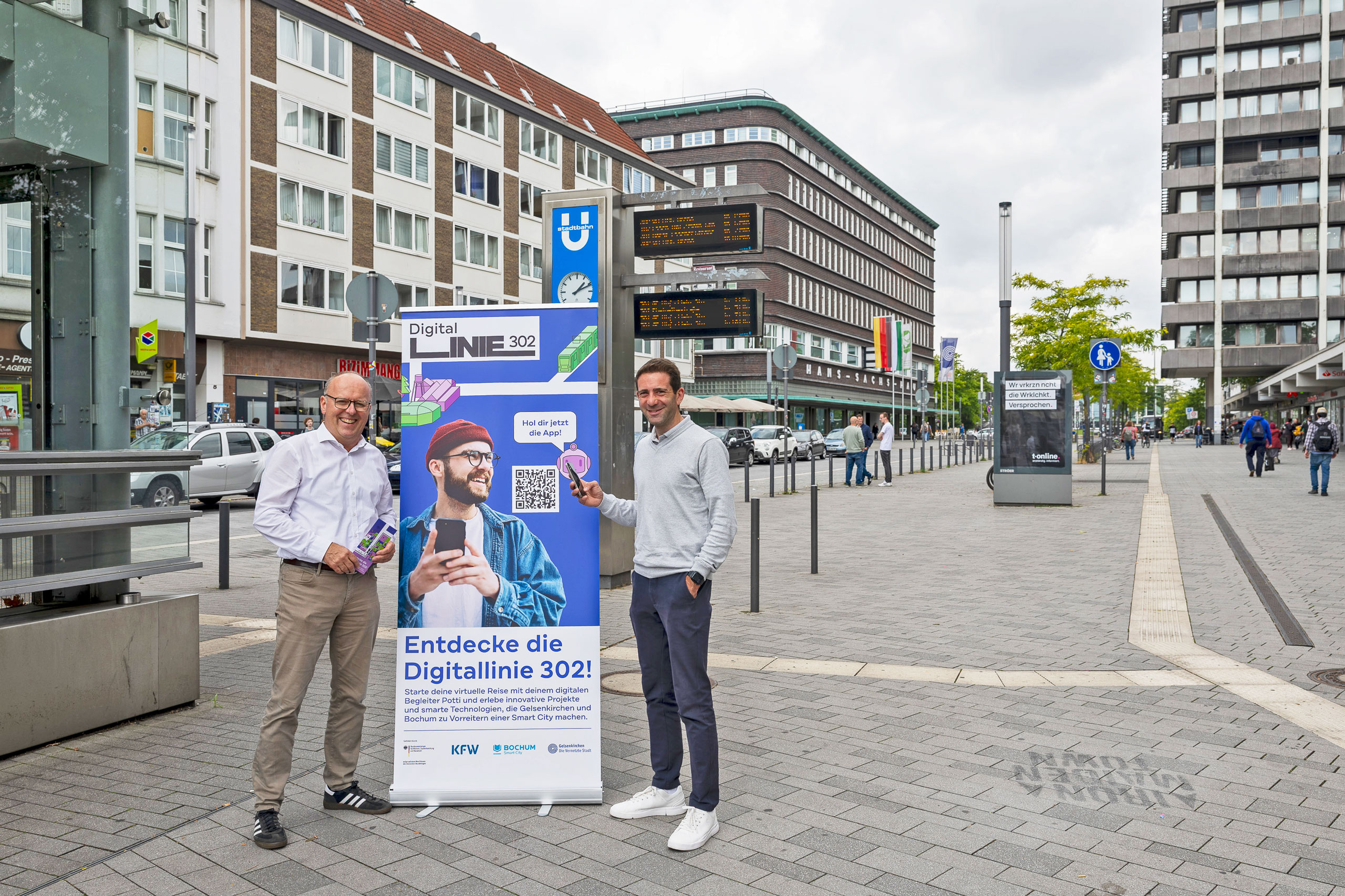 Zwei Personen stehen neben einem Werbeaufsteller für die Digitallinie 302.
