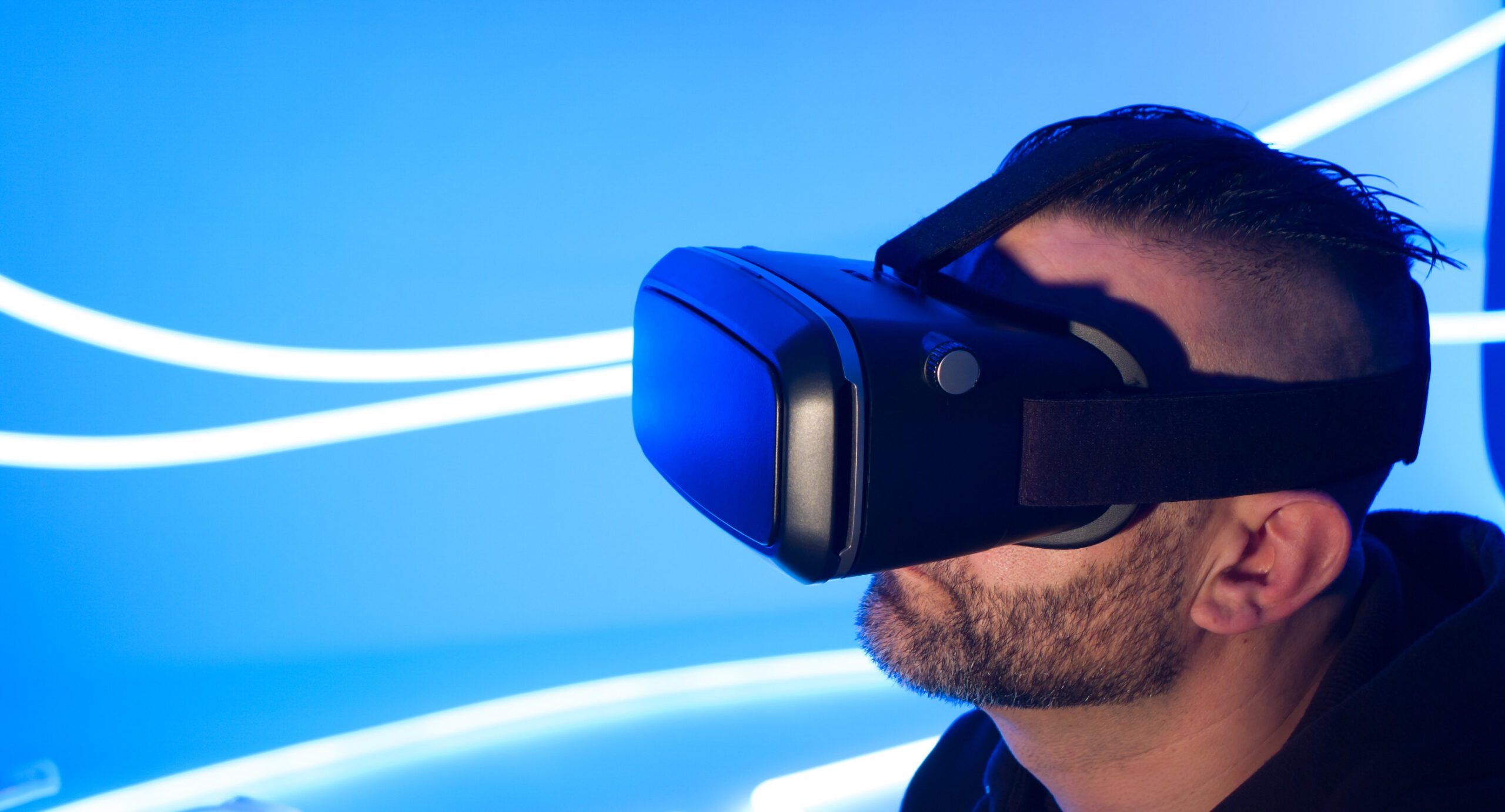 Porträtaufnahme eines jungen bärtigen Mannes mit VR-Brille vor blau-weißem Hintergrund