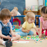 Drei Kleinkinder spielen mit Bauklötzen.