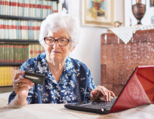 Eine ältere Frau sitzt an einem Laptop und schaut auf eine Kreditkarte.