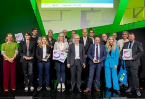 Gruppenfoto auf ener grün beleuchteten Bühne, einige Personen halten Urkunden in der Hand.