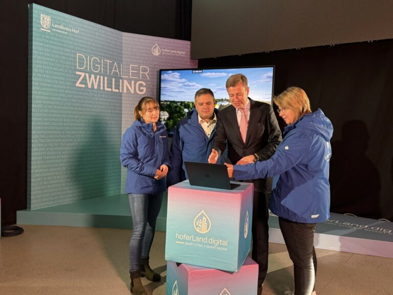 Vier Personen stehen in einem Ausstellungsraum um einen Laptop versammelt und betrachten dessen Bildschirm.