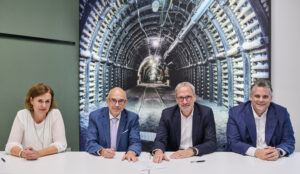 Vier Personen sitzen nebeneinander an einem Tisch, auf dem Vertragsunterlagen zu sehen sind.