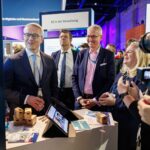 Mehrere Personen stehen in einem Messestand, vor ihnen auf dem Tisch stehen mehrere Tablets.