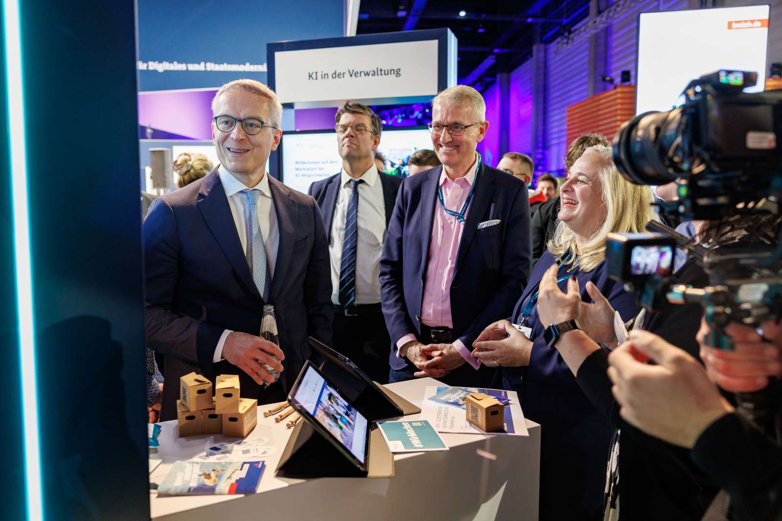 Mehrere Personen stehen in einem Messestand, vor ihnen auf dem Tisch stehen mehrere Tablets.
