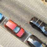 Draufsicht auf drei Autos, die auf einer Stadtstraße geparkt sind, zwei weitere Autos fahren vorbei.