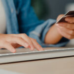 Eine Person hält eine Kreditkarte in der Hand, mit der anderen Hand tippt sie auf einer Computertastatur.