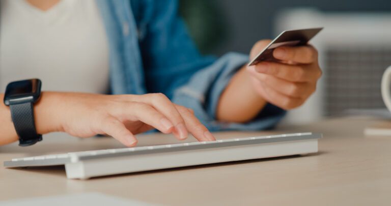 Eine Person hält eine Kreditkarte in der Hand, mit der anderen Hand tippt sie auf einer Computertastatur.