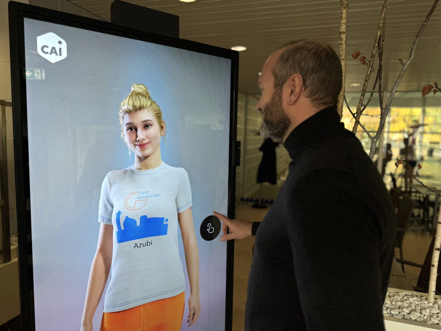 Ein Mann hantiert mit einem Bildschirm, auf dem ein weiblicher Avatar zu sehen ist.