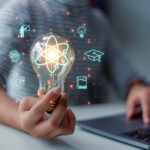 Hand, Arm und Oberkörper eines Schülers, der mit Laptop an einem Tisch sitzt, über der Hand schweben als Overlay Icons für die verschiedenen Schulfächer.