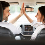Blick von der Rückbank auf den Fahrer und seine Beifahrerin, die High Five geben.