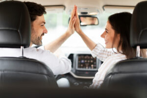 Blick von der Rückbank auf den Fahrer und seine Beifahrerin, die High Five geben.