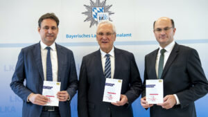 Die drei Minister stehen nebeneinander und halten je ein Exemplar des Berichts zur Cybersicherheit in Bayern 2025 in den Händen.