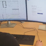Eine Person sitzt an einem Desktop-Rechner und arbeitet an einem Bauplan.