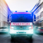 Ein Feuerwehrauto fährt mit Blaulicht auf einer Straße in einer Stadt.