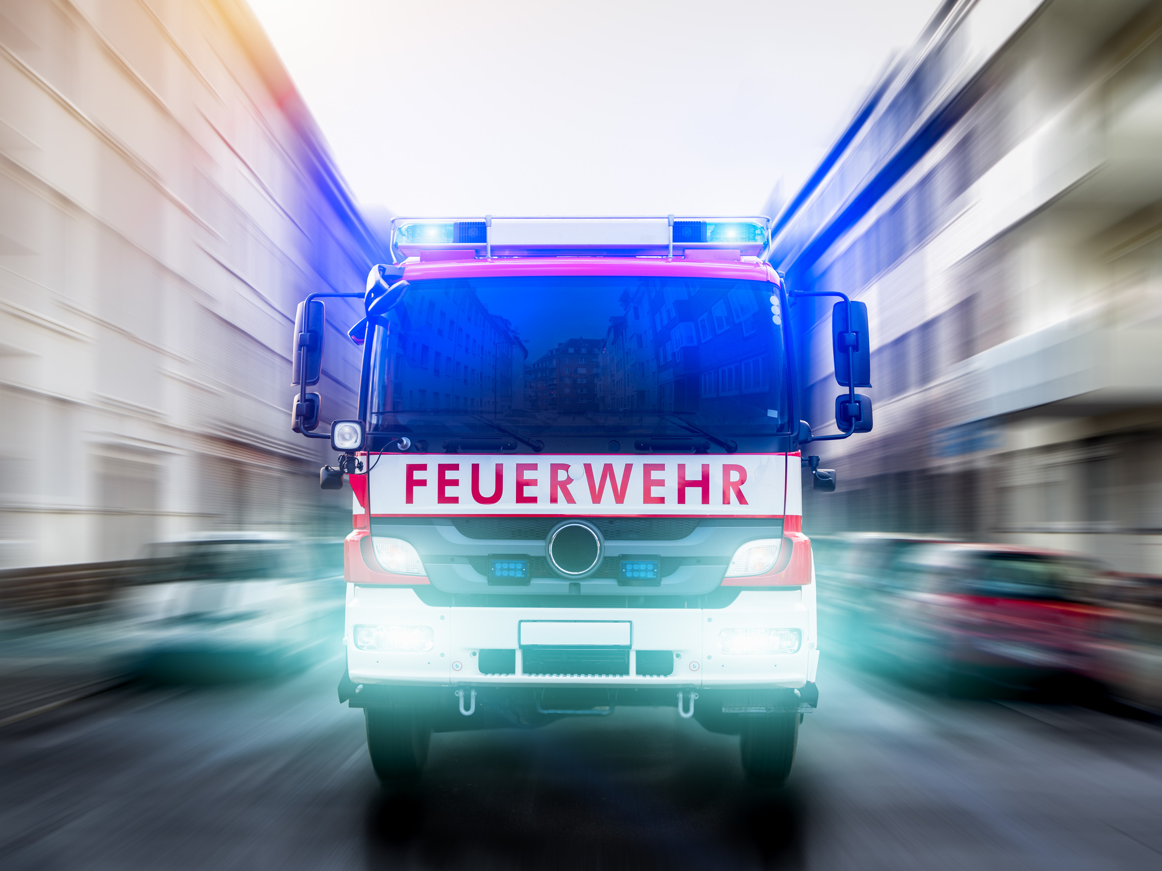 Ein Feuerwehrauto fährt mit Blaulicht auf einer Straße in einer Stadt.