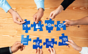 Sieben Hände halten je ein großes Puzzleteil, das mit den anderen Puzzleteilen verbunden werden soll.