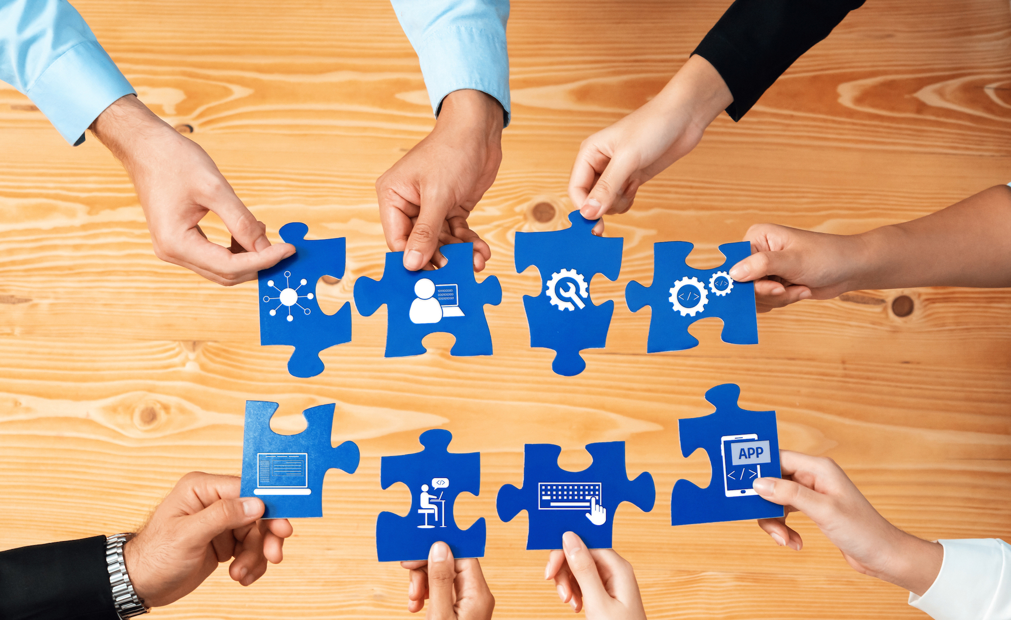 Sieben Hände halten je ein großes Puzzleteil, das mit den anderen Puzzleteilen verbunden werden soll.