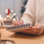 Frau schreibt auf einem Notizblock, im Hintergrund weihnachtliche Deko