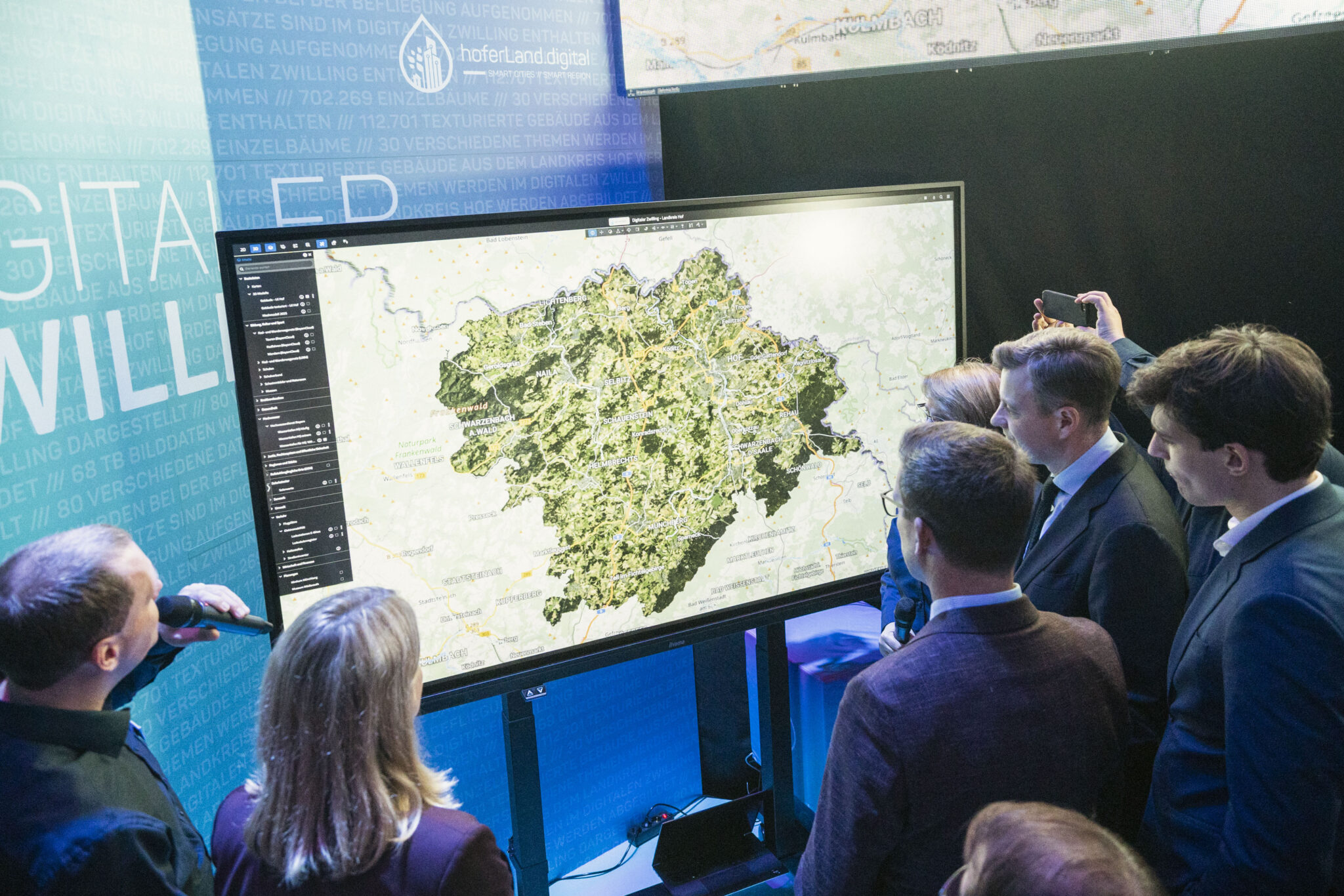 Mehrere Personen stehen um ein Smartboard versammelt, auf dem eine Landkarte zu sehen ist.