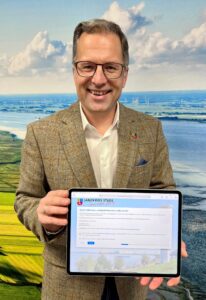 Der Landrat hält ein Tablet in den Händen, auf dessen Bildschirm die Onlineumfrage der Kreisverwaltung Stade zu sehen ist.