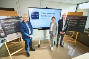 Drei Personen stehen vor einem großen Display und mehreren Präsentationswänden.