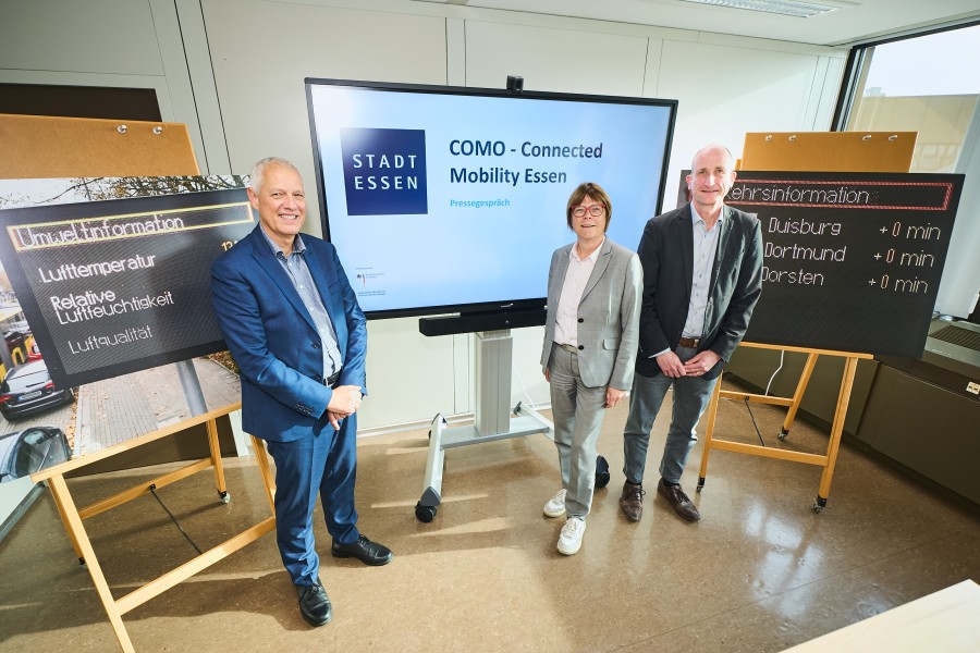 Drei Personen stehen vor einem großen Display und mehreren Präsentationswänden.