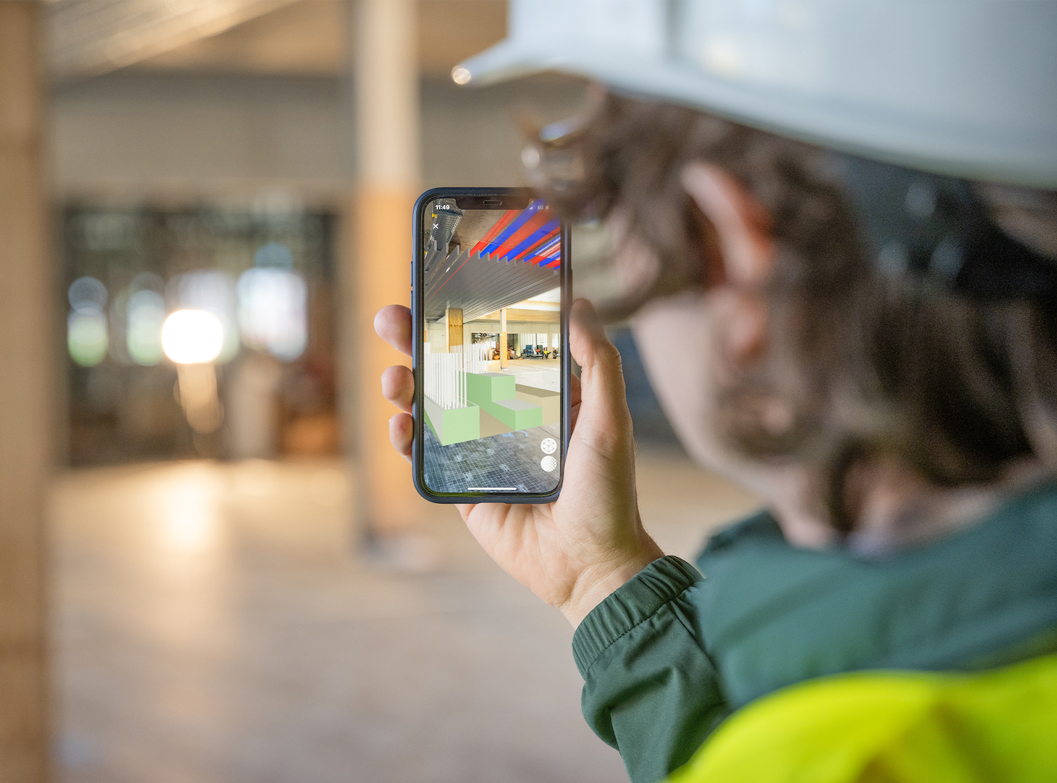 Eine Person mit Bauhelm hält ein Smartphone in der Hand auf dem die 3D_Darstellung eines Innenraums zu sehen ist.