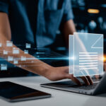 Eine Person arbeitet an Dokumenten und Ordnern auf einem Laptop.