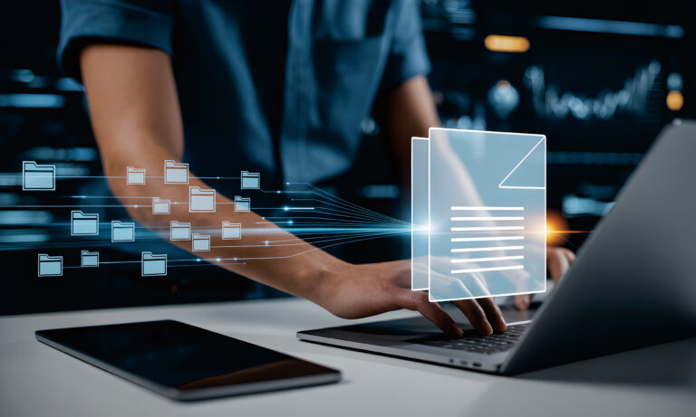 Eine Person arbeitet an Dokumenten und Ordnern auf einem Laptop.