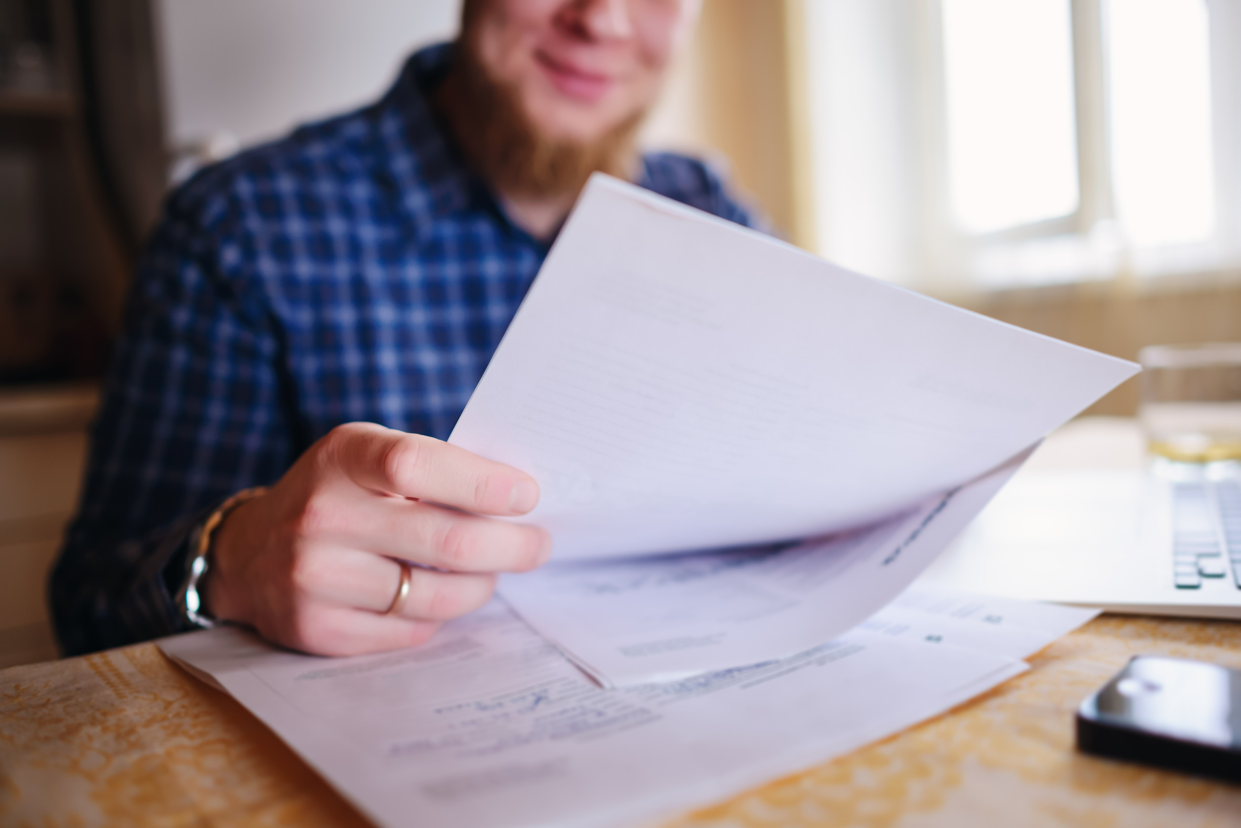 Mann am Schreibtisch mit Laptop, hantiert mit Papieren.