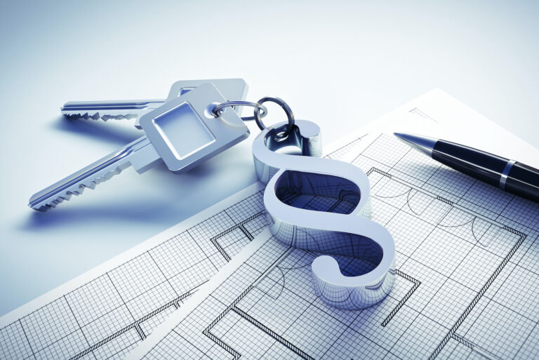Ein Schlüsselbund mit einem Anhänger in Paragrafenform liegt auf dem Grundriss eines Gebäudes.