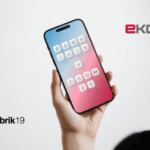 Eine Person hält ein Smartphone in der Hand auf dessen Bildschirm die Namen Fabrik19 und ekom21 zu sehen sind.