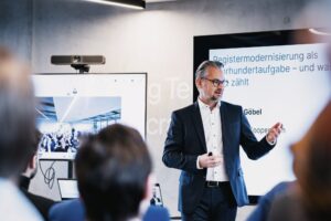 FITKO-Präsident André Göbel beim Vortrag, im Hintergrund ist eine Präsentation eingeblendet.