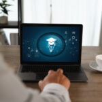 Eine Person sitzt vor einem aufgeklappten Laptop, auf dessen Bildschirm unterschiedliche Bildungssymbole zu sehen sind.
