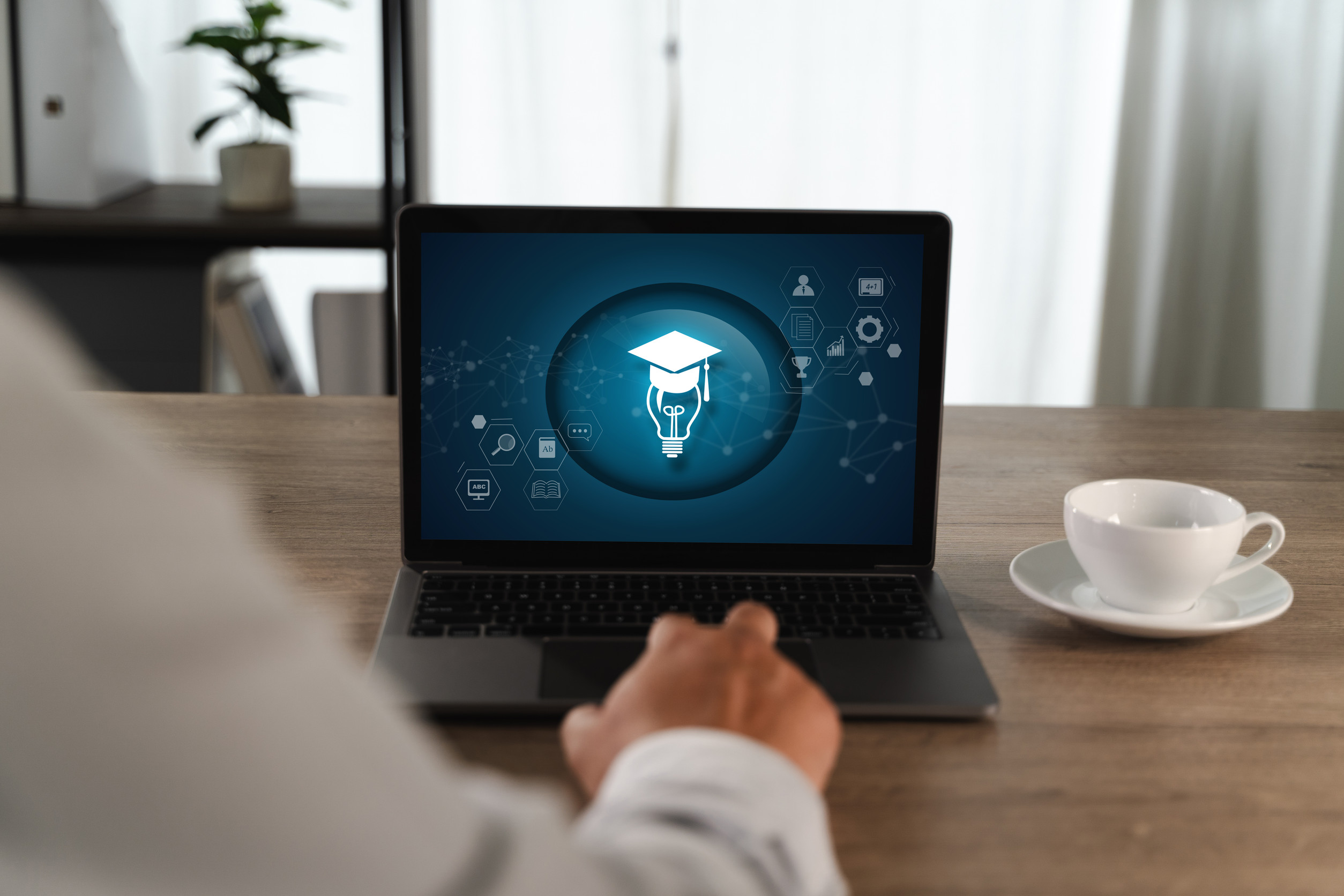 Eine Person sitzt vor einem aufgeklappten Laptop, auf dessen Bildschirm unterschiedliche Bildungssymbole zu sehen sind.