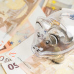 Ein durchsichtiges Sparschwein steht auf zahlreichen 50-Euro-Scheinen.