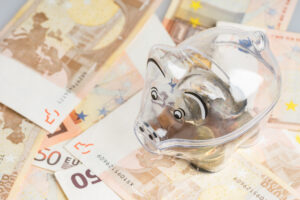 Ein durchsichtiges Sparschwein steht auf zahlreichen 50-Euro-Scheinen.