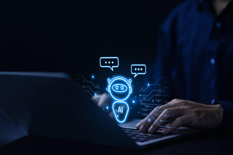 Eine Person sitzt an einem Laptop, über dessen Tastatur ein Chatbotsymbol schwebt.