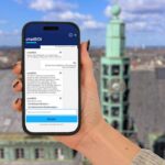 Eine Person hält ein Smartphone in der Hand, auf dessen Bildschirm ein Dialog mit dem Bochumer ChatBOt abgebildet ist. Im Hintergrund ist eine Luftaufnahme der Stadt Bochum zu erkennen.