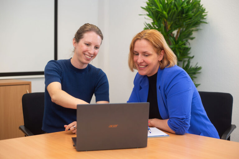 Maren Warnecke zeigt Mira Jago etwas auf dem Bildschirm eines Laptops.