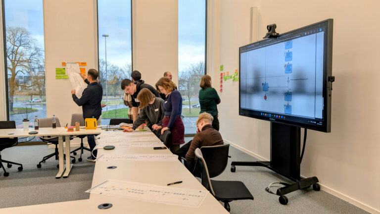 Mehrere jüngere Personen sind in einem Besprechungsraum mit einer Projektarbeit befasst.