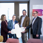 Mehrere Personen stehen nebeneinander in einem Raum und halten ein großes Plus-Symbol in der Hand, das die Zusammenarbeit von ProVitako und Unite markiert.