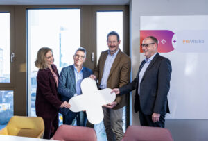 Mehrere Personen stehen nebeneinander in einem Raum und halten ein großes Plus-Symbol in der Hand, das die Zusammenarbeit von ProVitako und Unite markiert.