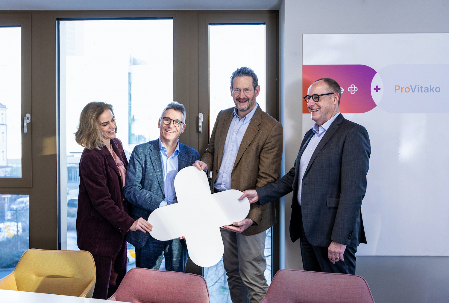 Mehrere Personen stehen nebeneinander in einem Raum und halten ein großes Plus-Symbol in der Hand, das die Zusammenarbeit von ProVitako und Unite markiert.