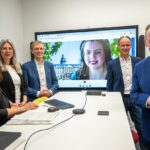 Start Videotelefonie in Karlsruhe, fünf Personen stehen am Tisch, Bildschirm im Hintergrund
