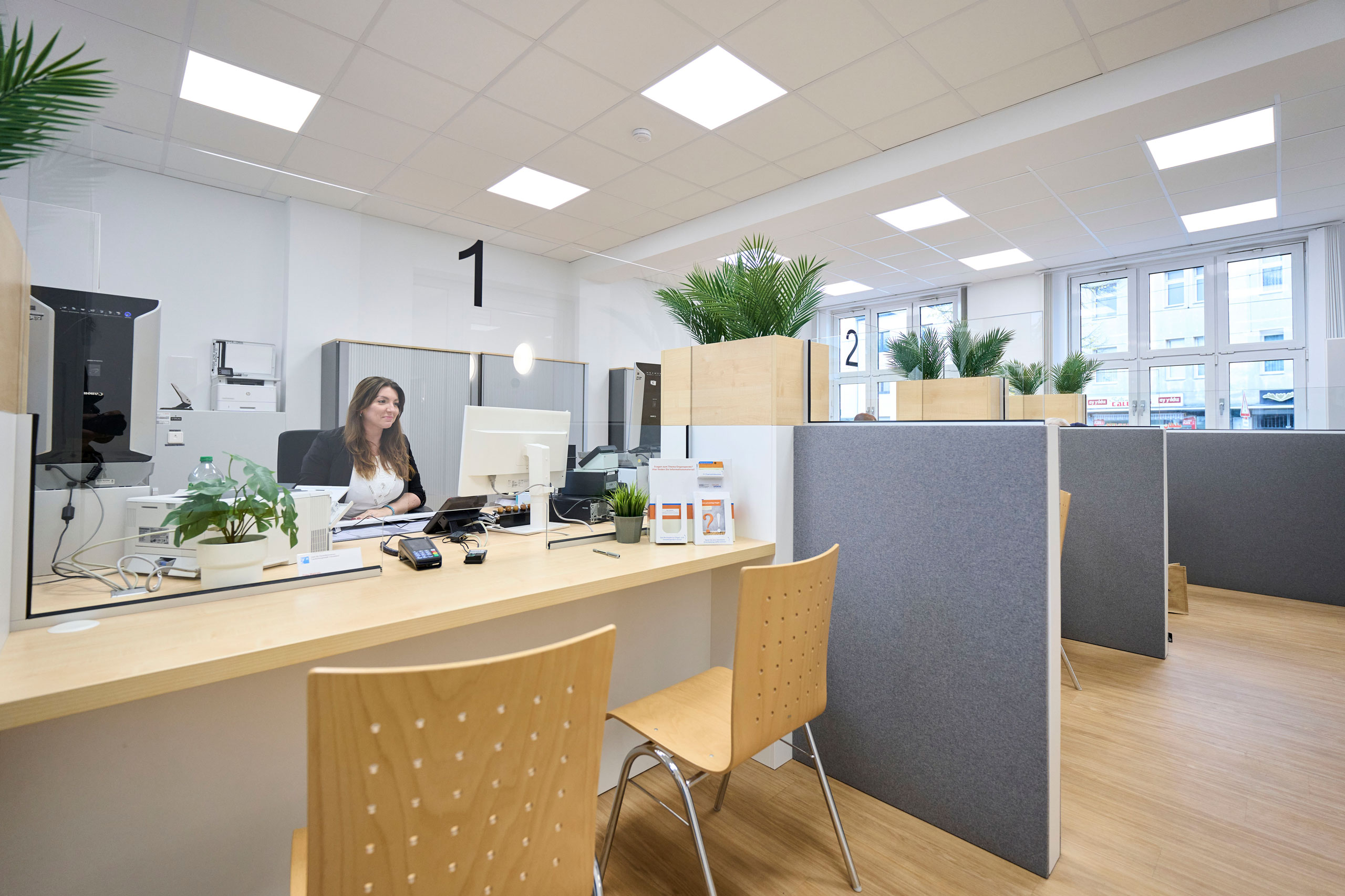 Eine Frau sitzt in einem Großraumbüro und arbeitet an einem Computer.