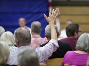 Mehrere Personen sitzen im Rahmen einer Veranstaltung zusammen und stimmen per Handzeichen über etwas ab.